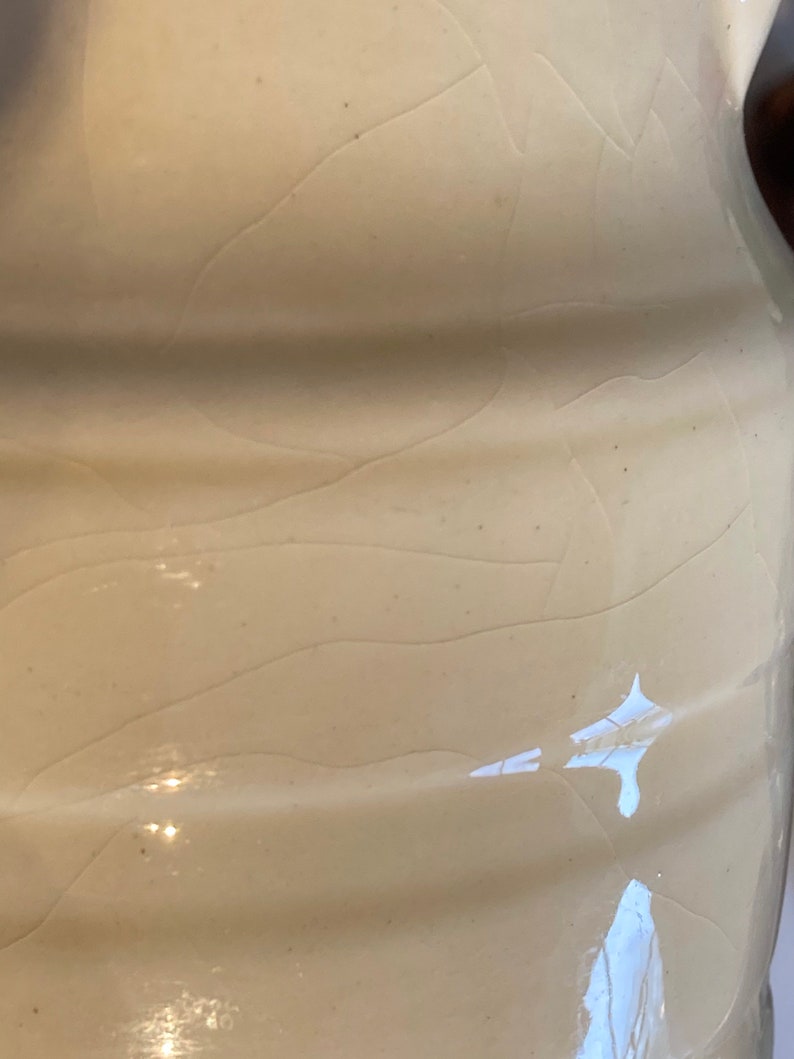 May include: A close-up of a white ceramic pitcher with a textured surface. The pitcher has a slightly rounded shape and a smooth, glossy finish.