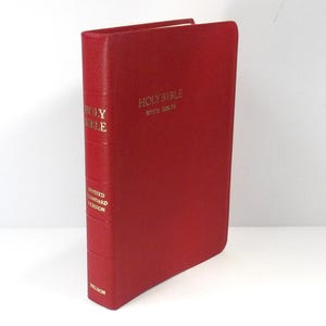 Puede incluir: Una Santa Biblia de tapa dura roja con letras doradas. El lomo dice "Holy Bible" y "Revised Standard Version". La portada también tiene las palabras "Holy Bible with Helps" en oro. Es una edición Nelson.