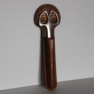 May include: A pair of silver scissors with a brown leather sheath. The scissors have the text "The Co. remarkable 5 193" and "county as & Ace 56 5" engraved on the blades.