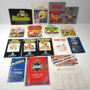 Peut inclure: Une collection de manuels d'instructions et de catalogues de jeux vidéo Atari vintage présentant des illustrations colorées pour des titres comme Frogger, Pac-Man, Ms. Pac-Man, Pitfall et Donkey Kong, avec une carte de garantie et des dépliants.