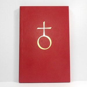 May include: A red book with a gold symbol on the cover. The symbol is a cross above a circle. The book is rectangular and appears to be hardcover.