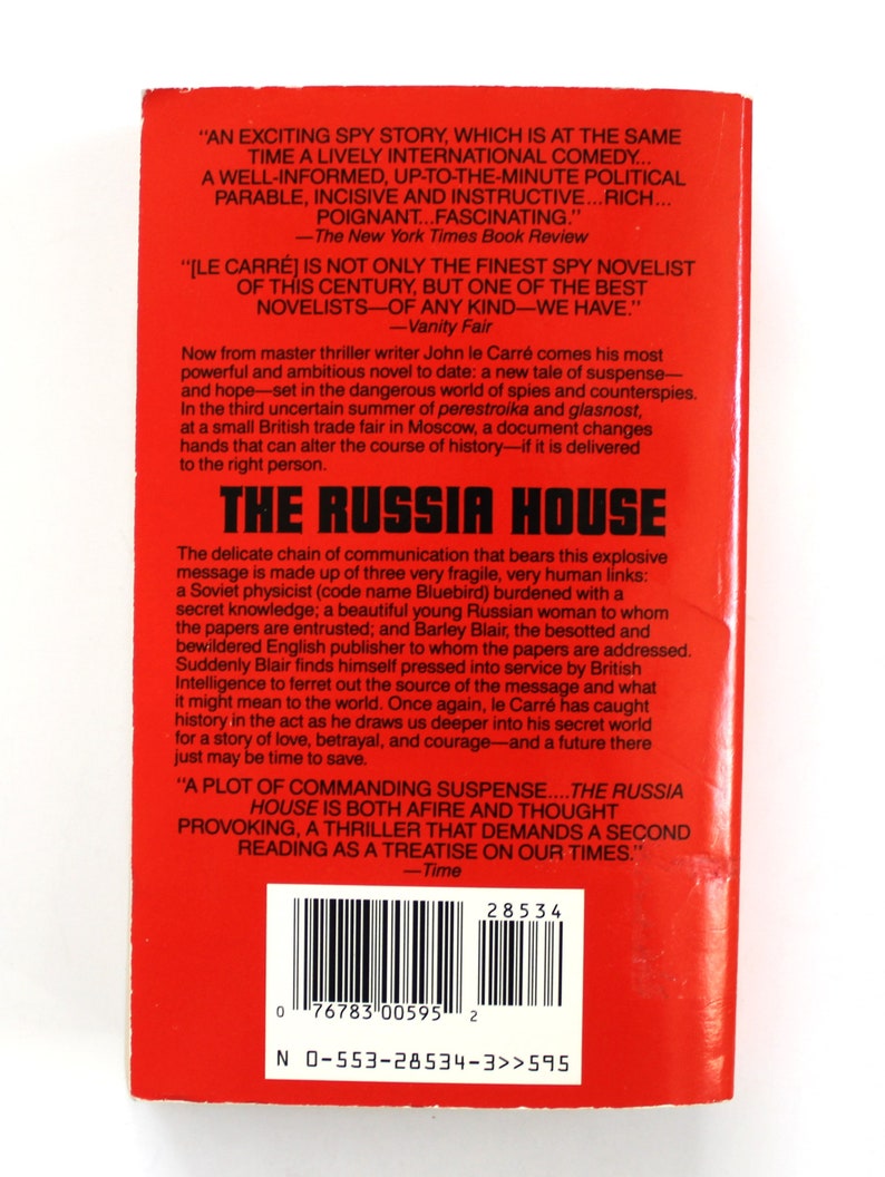 May include: A red paperback book cover with the title "The Russia House" in white text. The book is by John le Carre and features a quote from The New York Times Book Review and Vanity Fair.