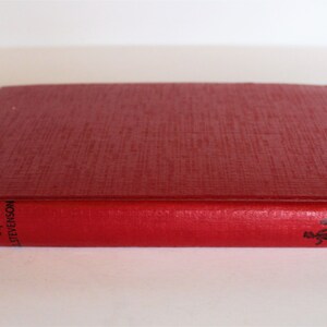 May include: A red hardcover book titled "The Black Arrow" by Robert Louis Stevenson. The book has a black and white illustration of two people walking on the spine.