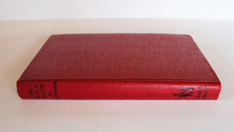 May include: A red hardcover book titled "The Black Arrow" by Robert Louis Stevenson. The book has a black and white illustration of two people walking on the spine.