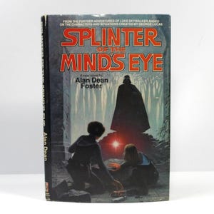 May include: A vintage paperback book titled "Splinter of the Mind's Eye" by Alan Dean Foster. The cover features a dark illustration of characters and a menacing figure, with the title in large, bold letters.
