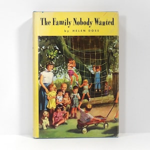 May include: Vintage hardcover book titled "The Family Nobody Wanted" by Helen Doss. The cover features a colorful illustration of children playing on a jungle gym, with adults and a dog nearby. The book has a yellow spine.