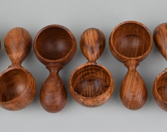 May include: A collection of handcrafted wooden measuring scoops. Each scoop features a rounded bowl and a teardrop-shaped handle, all made from a rich, dark wood with visible grain patterns. The scoops are arranged in a row against a neutral background.