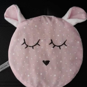 Puede incluir: Juguete de peluche rosa con forma de animal durmiendo con estrellas blancas y ojos negros. El juguete tiene una pequeña nariz negra y pelaje blanco alrededor de las orejas.