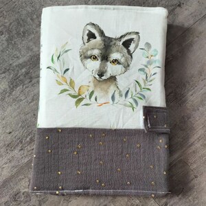 May include: A gray and white fabric book cover with a watercolor illustration of a wolf pup surrounded by green leaves. The bottom half of the cover is a dark gray fabric with gold polka dots.