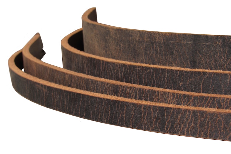 May include: Close-up of three pieces of brown leather straps stacked on top of each other. The leather has a distressed look with a dark brown color and a light brown edge.