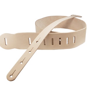 May include: A natural-colored leather guitar strap. The strap has a wide, padded section for the shoulder and a narrower adjustable section with multiple adjustment slots and holes. The strap is designed to be durable and comfortable for extended use.