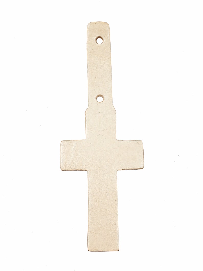 May include: A white leather cross with two holes at the top and one in the middle. The cross is a decorative piece and can be used for crafts.
