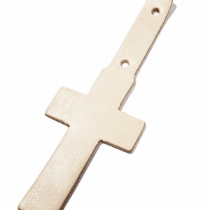 May include: A white leather cross with two holes punched through the top. The cross is designed to be used as a strap or belt loop.