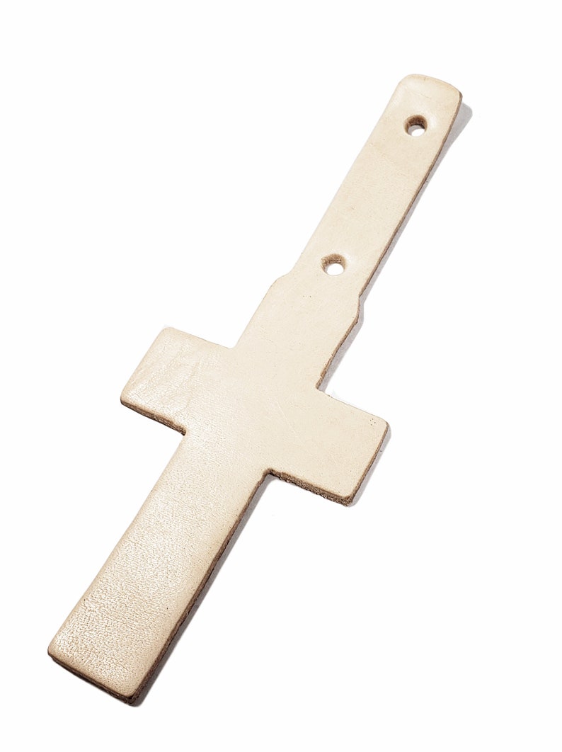 May include: A white leather cross with two holes punched through the top. The cross is designed to be used as a strap or belt loop.