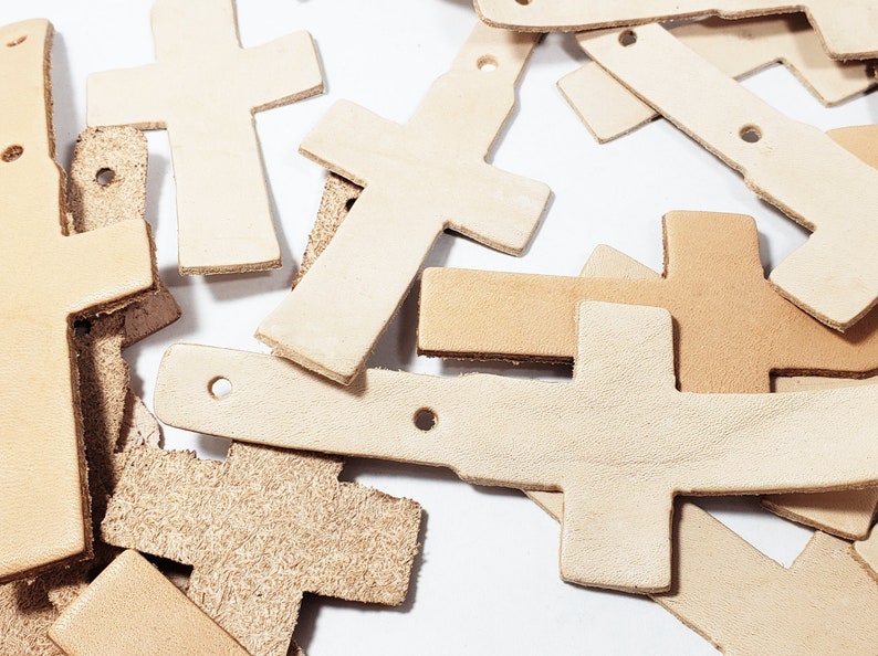 May include: A pile of leather cross shapes in various sizes and shades of brown. The crosses are cut out and ready to be used for crafting projects.