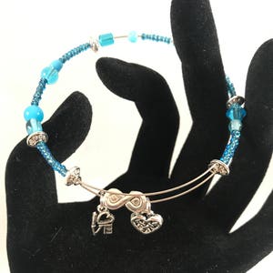 Puede incluir: Una pulsera de cuentas azules con detalles y dijes plateados. La pulsera presenta una mezcla de cuentas azules claras y oscuras, con detalles de metal plateado. Los dijes incluyen la palabra "LOVE" y un corazón.
