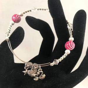 Puede incluir: Un brazalete de plata con cuentas rosas y plateadas, un dije de estrella, un dije de corazón y un dije de cisne.