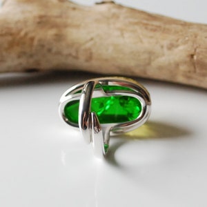 K&ouml;nnte beinhalten: Ein silberner Ring mit einem gro&szlig;en ovalen Edelstein in Gr&uuml;n- und Gelbt&ouml;nen. Der Ring hat ein einzigartiges Design, bei dem die Ringschiene um den Stein gewickelt ist.