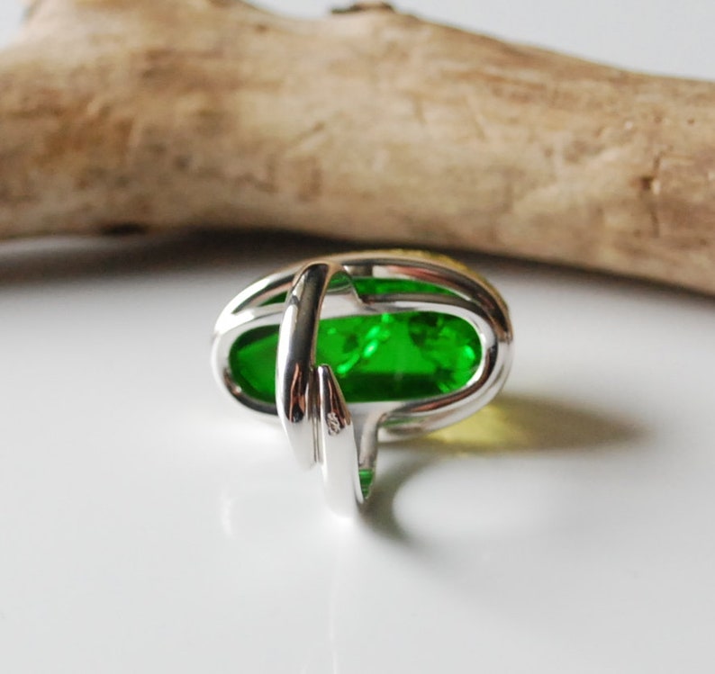 K&ouml;nnte beinhalten: Ein silberner Ring mit einem gro&szlig;en ovalen Edelstein in Gr&uuml;n- und Gelbt&ouml;nen. Der Ring hat ein einzigartiges Design, bei dem die Ringschiene um den Stein gewickelt ist.