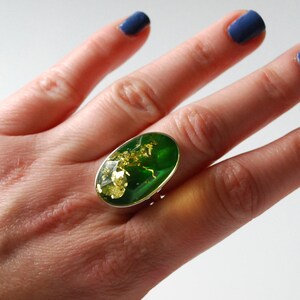 K&ouml;nnte beinhalten: Ein silberner Ring mit einem gro&szlig;en ovalen gr&uuml;nen Stein, der in der Mitte sitzt. Der Stein hat goldene Flecken.
