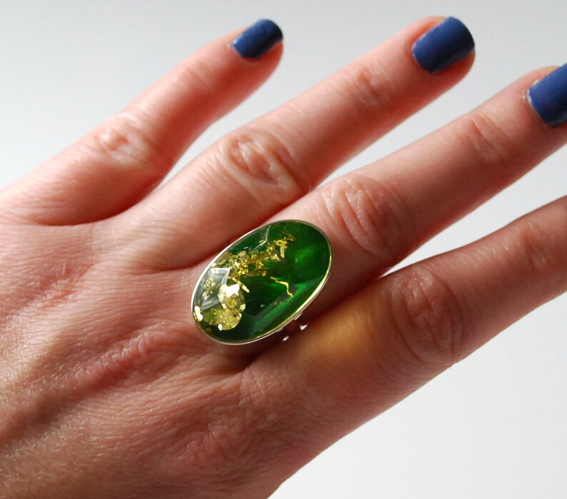 K&ouml;nnte beinhalten: Ein silberner Ring mit einem gro&szlig;en ovalen gr&uuml;nen Stein, der in der Mitte sitzt. Der Stein hat goldene Flecken.