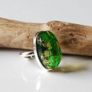 K&ouml;nnte beinhalten: Ein silberner Ring mit einem ovalen, gr&uuml;nen Stein, der in einer silbernen Fassung sitzt. Der Stein hat eine gr&uuml;ne und goldene Farbe und scheint Einschl&uuml;sse zu haben.