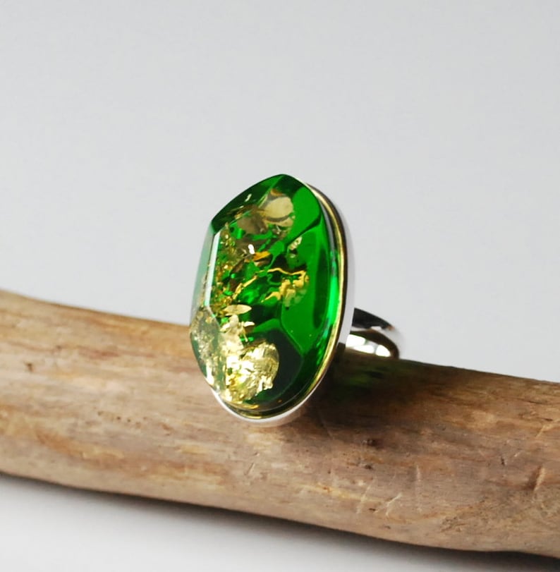 K&ouml;nnte beinhalten: Ein silberner Ring mit einem gro&szlig;en, ovalen, gr&uuml;nen Edelstein. Der Edelstein ist mit goldenen Flocken durchsetzt.