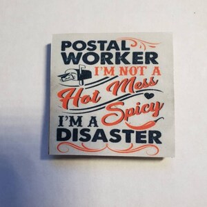 May include: A white sign with black and orange text that reads "Postal Worker I'm not a Hot Mess I'm a Spicy Disaster". The sign has a small red heart and a red chili pepper graphic.