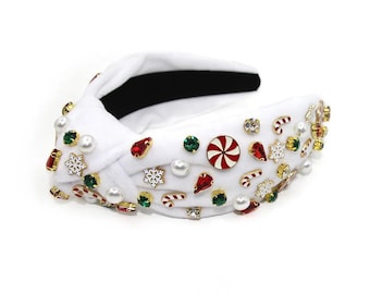 Op de afbeelding: Een witte hoofdband met een geknoopt ontwerp, versierd met rode, groene en witte kerstversieringen, waaronder snoepstokken, sneeuwvlokken en pepermuntjes.