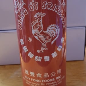 Puede incluir: Un recipiente cilíndrico rojo y verde con un logotipo de gallo blanco y el texto "Huy Fong Foods, Inc." y "Sriracha Hot Chili Sauce" impreso en la etiqueta. El recipiente es de 17 onzas (1 libra 1 onza) o 482 gramos.
