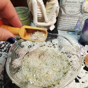May include: A white ceramic figurine of two skeletons kissing, a glass bowl filled with white salt crystals, and a bag of protection salt with the text "Protection Salt" and "Net Wt. 16 Oz (453g)".