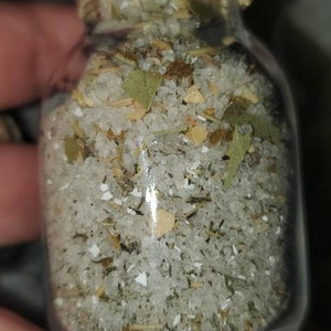 May include: A glass jar with a cork lid filled with white salt, dried herbs, and small pieces of dried fruit.