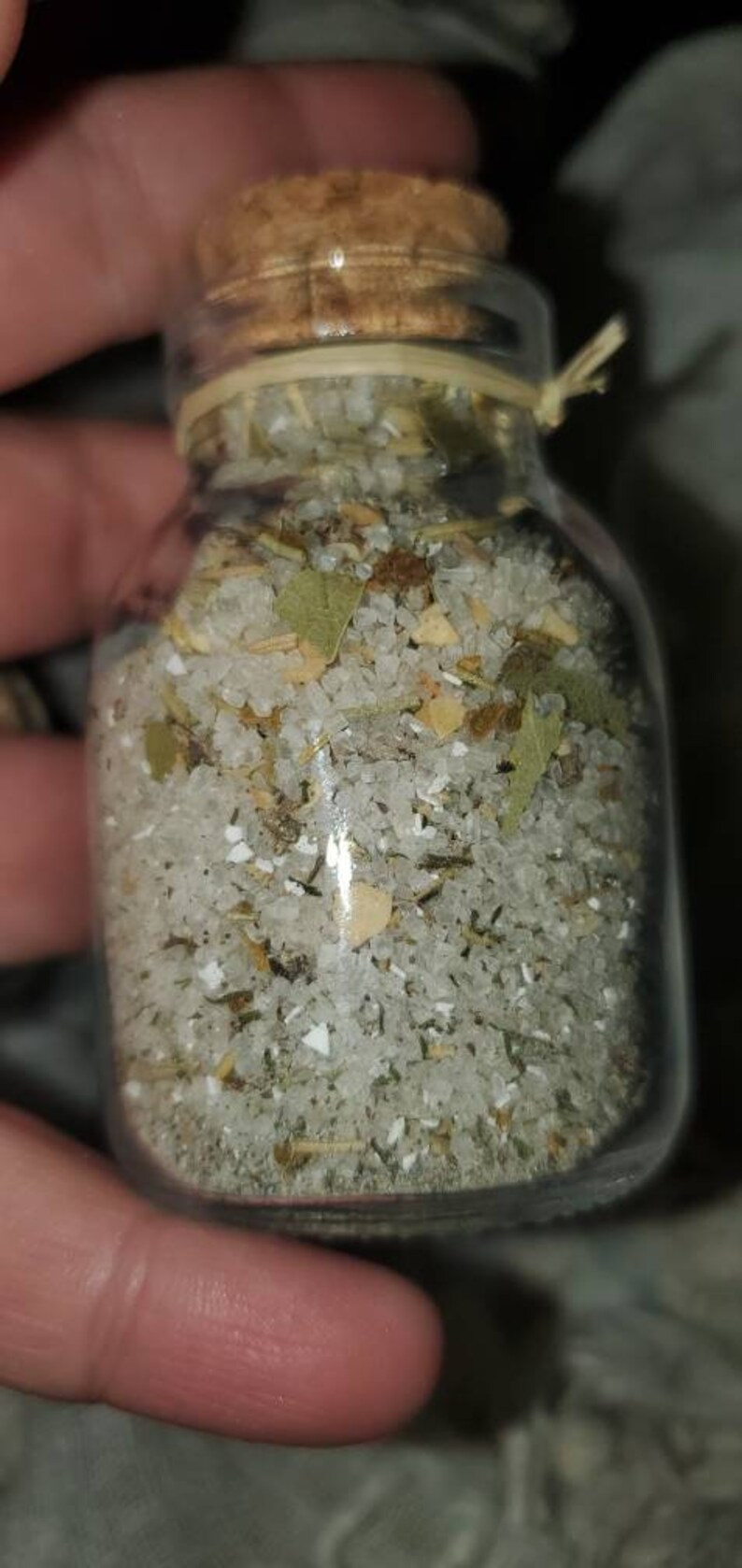 May include: A glass jar with a cork lid filled with white salt, dried herbs, and small pieces of dried fruit.