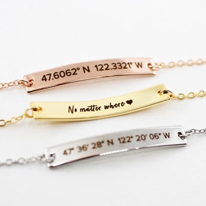 May include: Three gold bar necklaces with different engravings. The top necklace has the coordinates "47.6062° N 122.3321° W". The middle necklace has the text "No matter where" with a heart symbol. The bottom necklace has the coordinates "47 36 28" N 122° 20′06″ W".