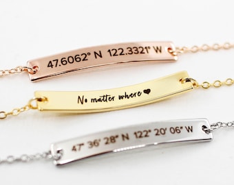 May include: Three gold bar necklaces with different engravings. The top necklace has the coordinates "47.6062° N 122.3321° W". The middle necklace has the text "No matter where" with a heart symbol. The bottom necklace has the coordinates "47 36 28" N 122° 20′06″ W".