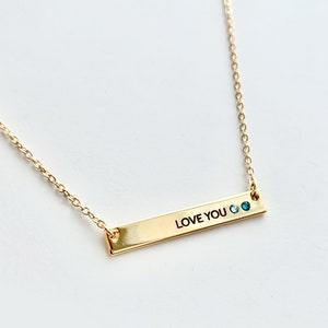 May include: Gold necklace with a bar pendant that says "LOVE YOU" with two blue gemstones.