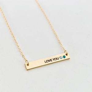 May include: Gold bar necklace with the words "LOVE YOU" engraved on it. The necklace has two small blue gemstones.