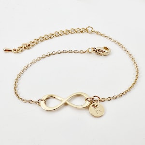 May include: A gold infinity symbol charm bracelet with a small gold charm with the letter 'R' on it.