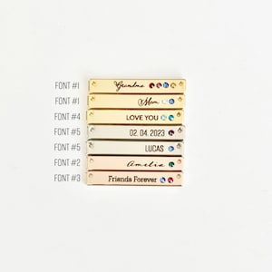 May include: A set of seven gold, silver, and rose gold bar pendants with various engraved text and rhinestones. The text includes "Grandma", "Mom", "Love You", "02.04.2023", "Lucas", "Amelia", and "Friends Forever".