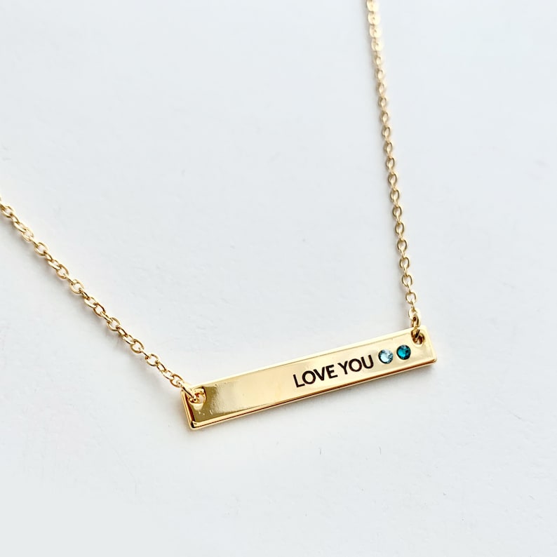May include: Gold necklace with a bar pendant that says "LOVE YOU" with two blue gemstones.