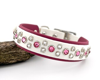 Puede incluir: Collar para perros blanco con detalles de cristales rosas y transparentes. El collar tiene un interior burdeos y está adornado con múltiples cristales rosas y transparentes. El collar es de cuero y tiene una hebilla plateada.