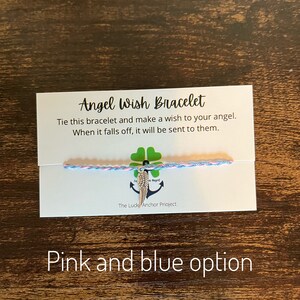 May include: A pink and blue string bracelet with a silver angel wing charm. The card reads "Angel Wish Bracelet" and "Tie this bracelet and make a wish to your angel. When it falls off, it will be sent to them." The card also says "The Luck Anchor Project".