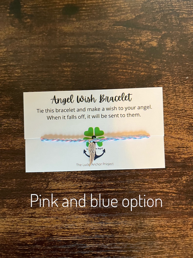 May include: A pink and blue string bracelet with a silver angel wing charm. The card reads "Angel Wish Bracelet" and "Tie this bracelet and make a wish to your angel. When it falls off, it will be sent to them." The card also says "The Luck Anchor Project".
