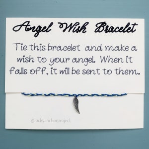 May include: A white card with blue and green string tied around it. The string has a silver angel wing charm attached. The card reads "Angel Wish Bracelet" and "Tie this bracelet and make a wish to your angel. When it falls off, it will be sent to them." The card also has the text "@luckyanchorproject" at the bottom.
