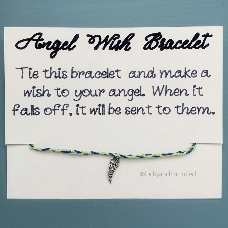 May include: A white card with black text that reads "Angel Wish Bracelet". The text continues, "Tie this bracelet and make a wish to your angel. When it falls off, it will be sent to them." A blue and green string bracelet with a silver angel wing charm is attached to the card. The text "@luckyanchorproject" is at the bottom of the card.