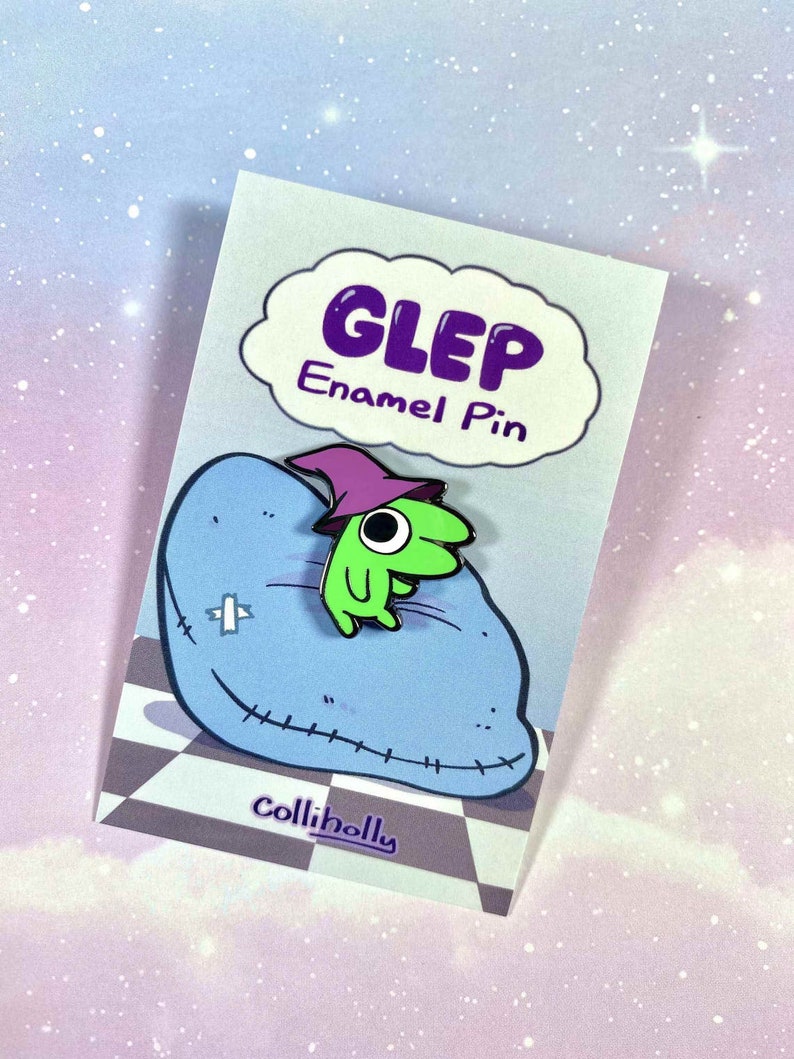 May include: Green and purple enamel pin of a cartoon creature wearing a purple hat, sitting on a blue pillow with stitching. The pin says "GLEP Enamel Pin" in a white speech bubble.
