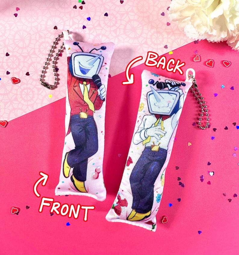 May include: Two rectangular plush keychains with a cartoon TV-headed character. One keychain shows the front of the character in a red jacket, blue pants, and yellow shoes, holding a microphone. The other keychain shows the back of the character in a white shirt and blue pants.