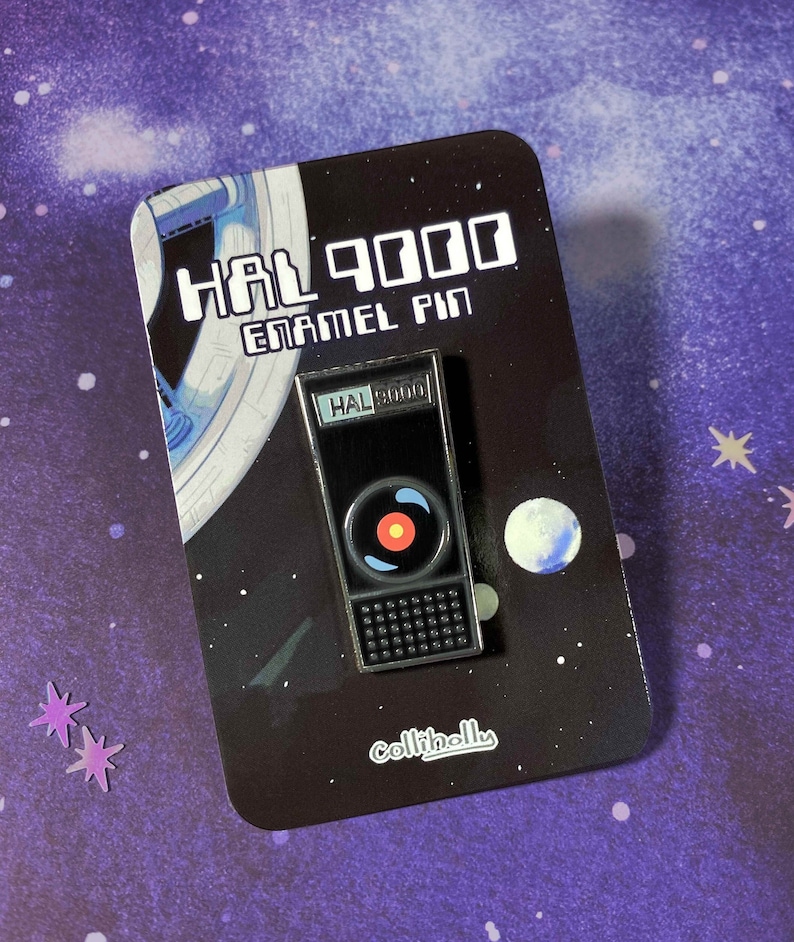 May include: A black enamel pin featuring a depiction of HAL 9000 from the movie 2001: A Space Odyssey. The pin is on a black card with white text that reads "HAL 9000 Enamel Pin" and "collitholis".
