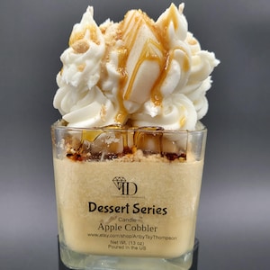 Puede incluir: Una vela de vidrio transparente con un aroma a pastel de manzana blanco y marrón. La vela está cubierta con una crema batida blanca y un chorrito de caramelo. La etiqueta dice "Dessert Series Candle Apple Cobbler" e incluye el sitio web www.etsy.com/shop/ArtbyTayThompson, Net Wt. (13 oz) y Poured in the US.