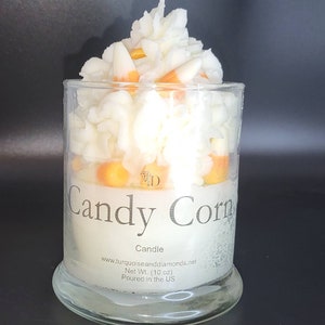 May include: A white candle with a candy corn scent. The candle is in a clear glass jar and is topped with a white wax design that resembles candy corn. The jar has a label that reads "Candy Corn Candle" and includes the website address "www.turquoiseanddiamonds.net", the net weight of 10 ounces, and the statement "Poured in the US".